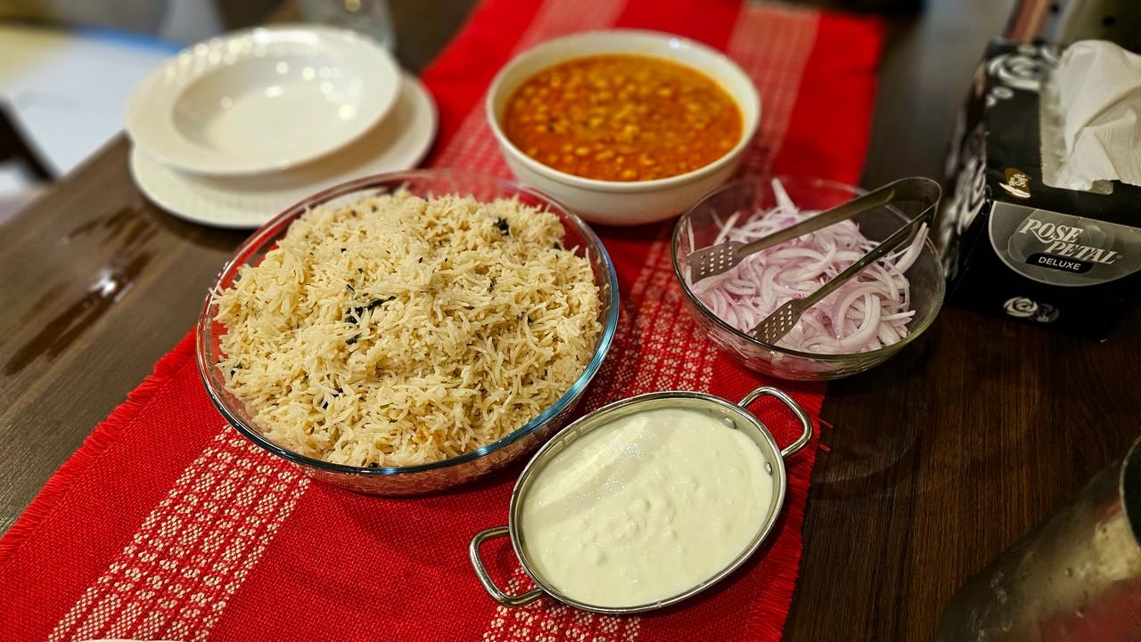 About Indian cuisine setting with basmati rice, curry, onion salad, and yogurt on a red tablecloth.